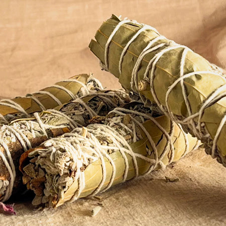 Three rolled sage smudge sticks tied with white string on a beige background