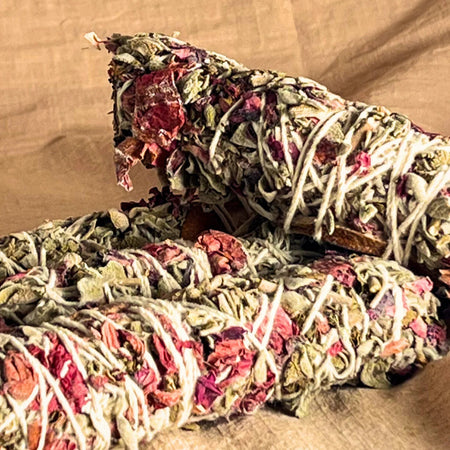 Two bundles of sage smudge sticks with red and green leaves on a brown background