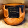 Copper-colored candle with a label on a textured fabric background