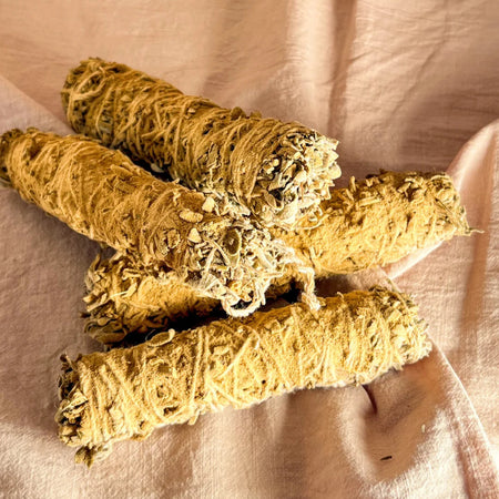 Three rolled-up sage smudge sticks on a soft pink fabric background