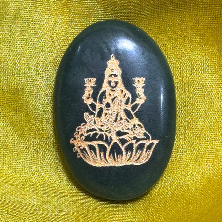 Black stone with gold embossed design of a seated figure on a yellow fabric background