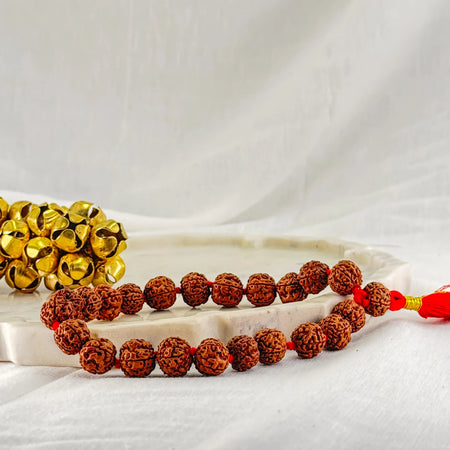 Two beaded bracelets, one gold and one brown, on a white fabric background.