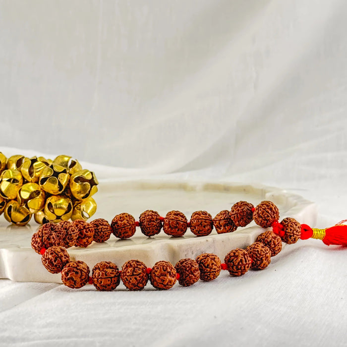 Two beaded bracelets, one gold and one brown, on a white fabric background.