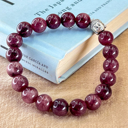 Red beaded bracelet with a silver Buddha charm on a book