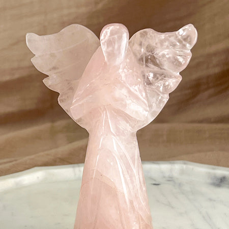 Pink angel sculpture on a marble surface with a wooden background