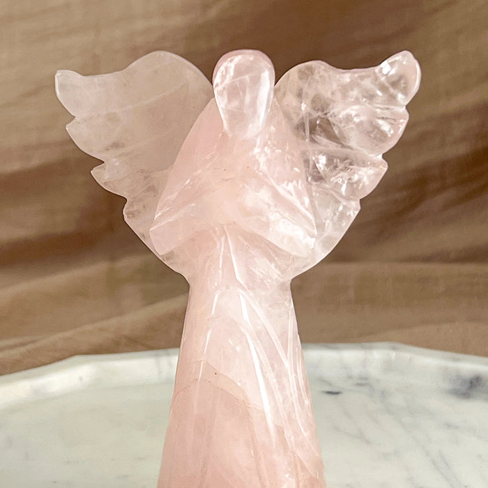 Pink angel sculpture on a marble surface with a wooden background
