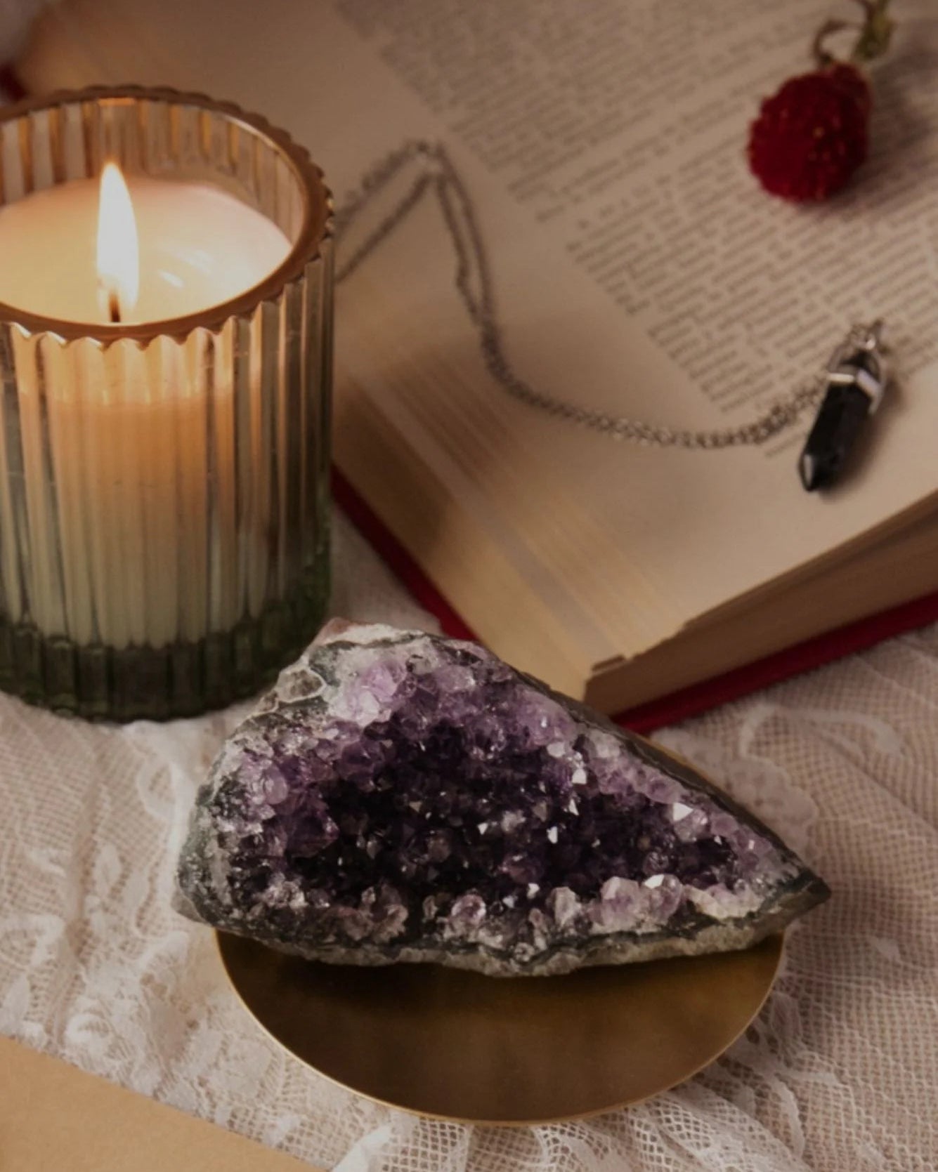 Amethyst crystal, lit candle, and necklace on an open book